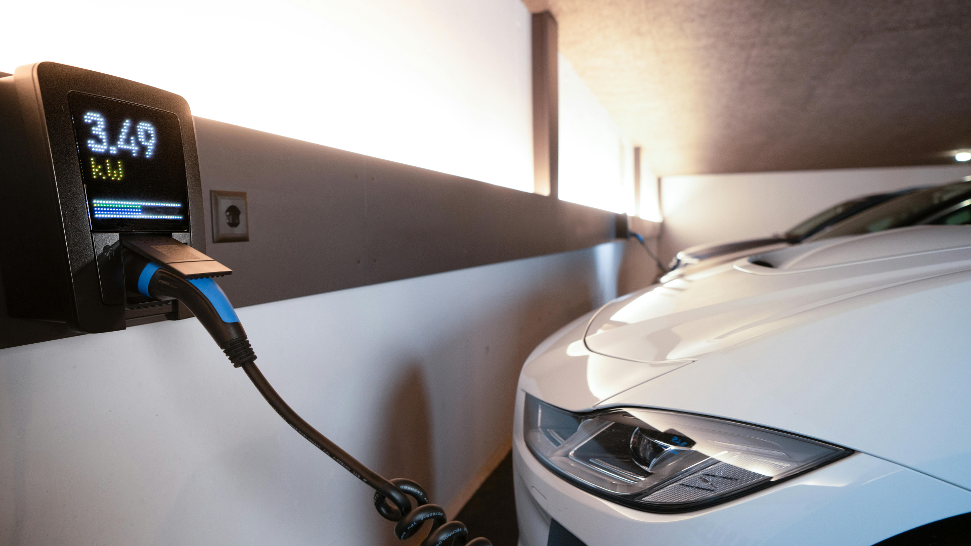 Coche eléctrico moderno conectado a un cargador mural inteligente en un garaje. Instalación de cargador para vehículo eléctrico en garaje.